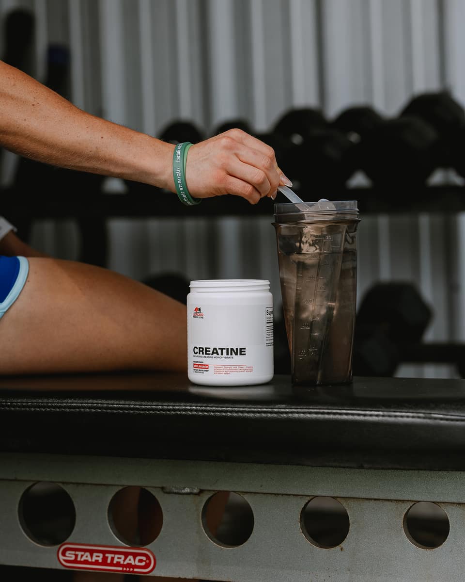 Scooping creatine into a shaker on a gym bench