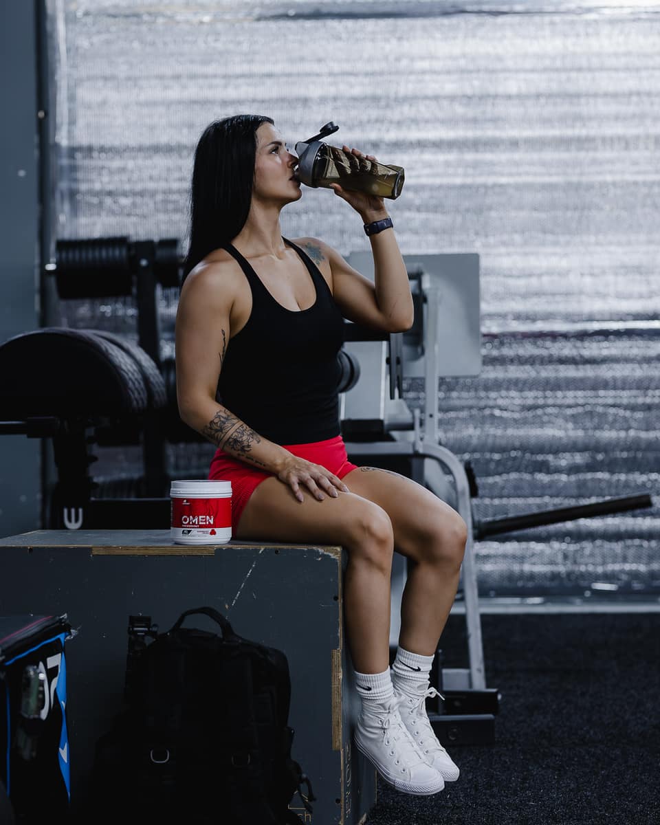 Athlete resting with a shaker and OMEN pre-workout in the gym